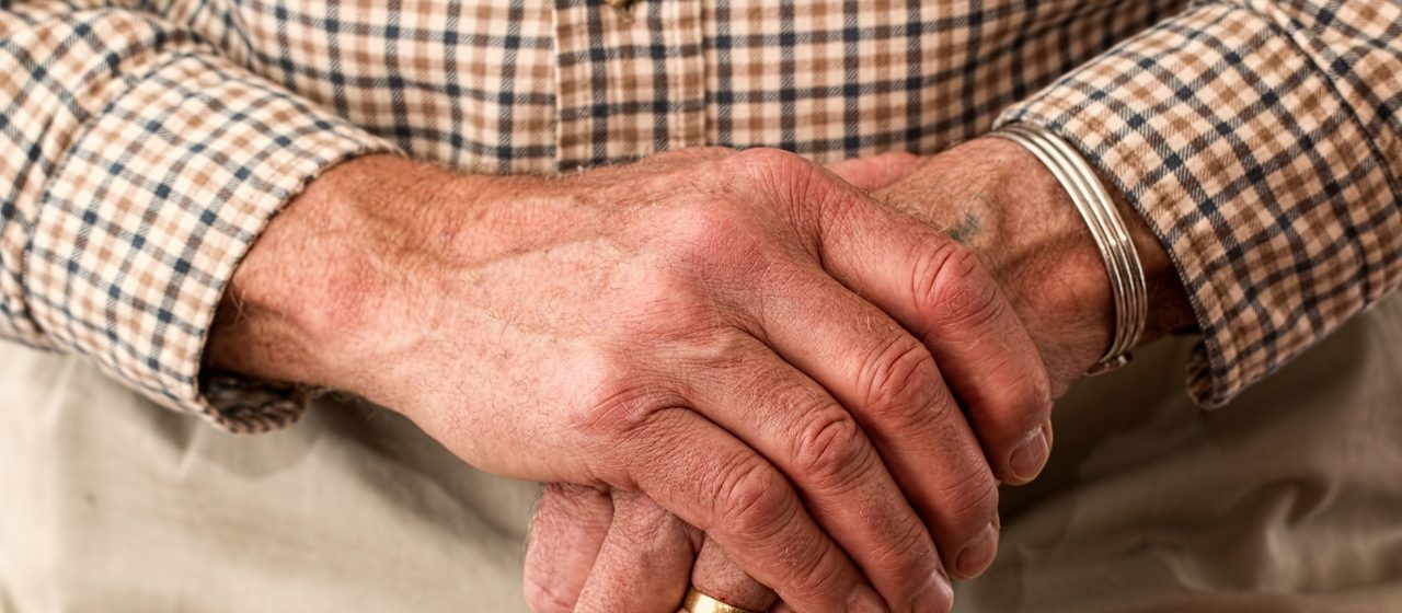 Starszy człowiek z obrączką trzyma laskę w ręku.